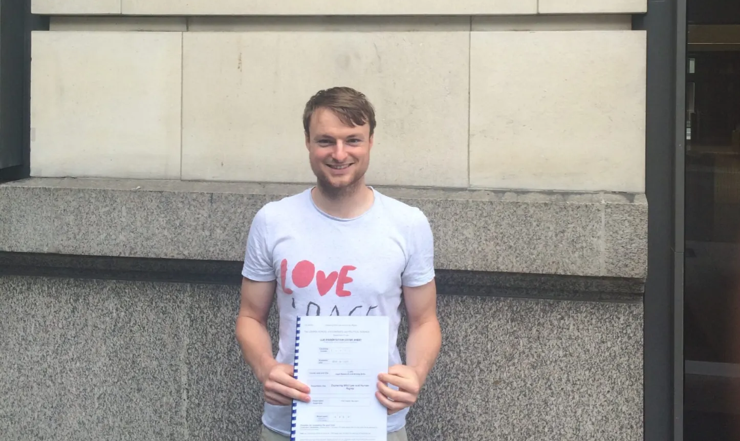 Picture shows me holding my dissertation in front of a wall